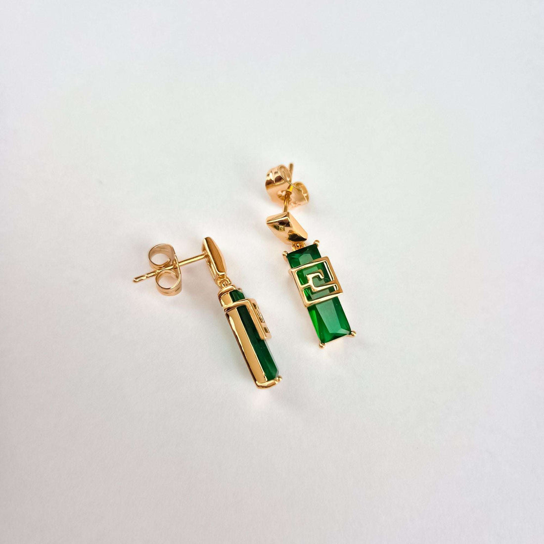 Zaļo akmeņu auskaru pāris slīpā rakursā ar apzeltītu stienīša aizdari