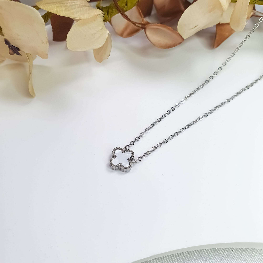 Balta āboliņa piekariņa sānskats ar lodīšu apmali uz gaišas virsmas