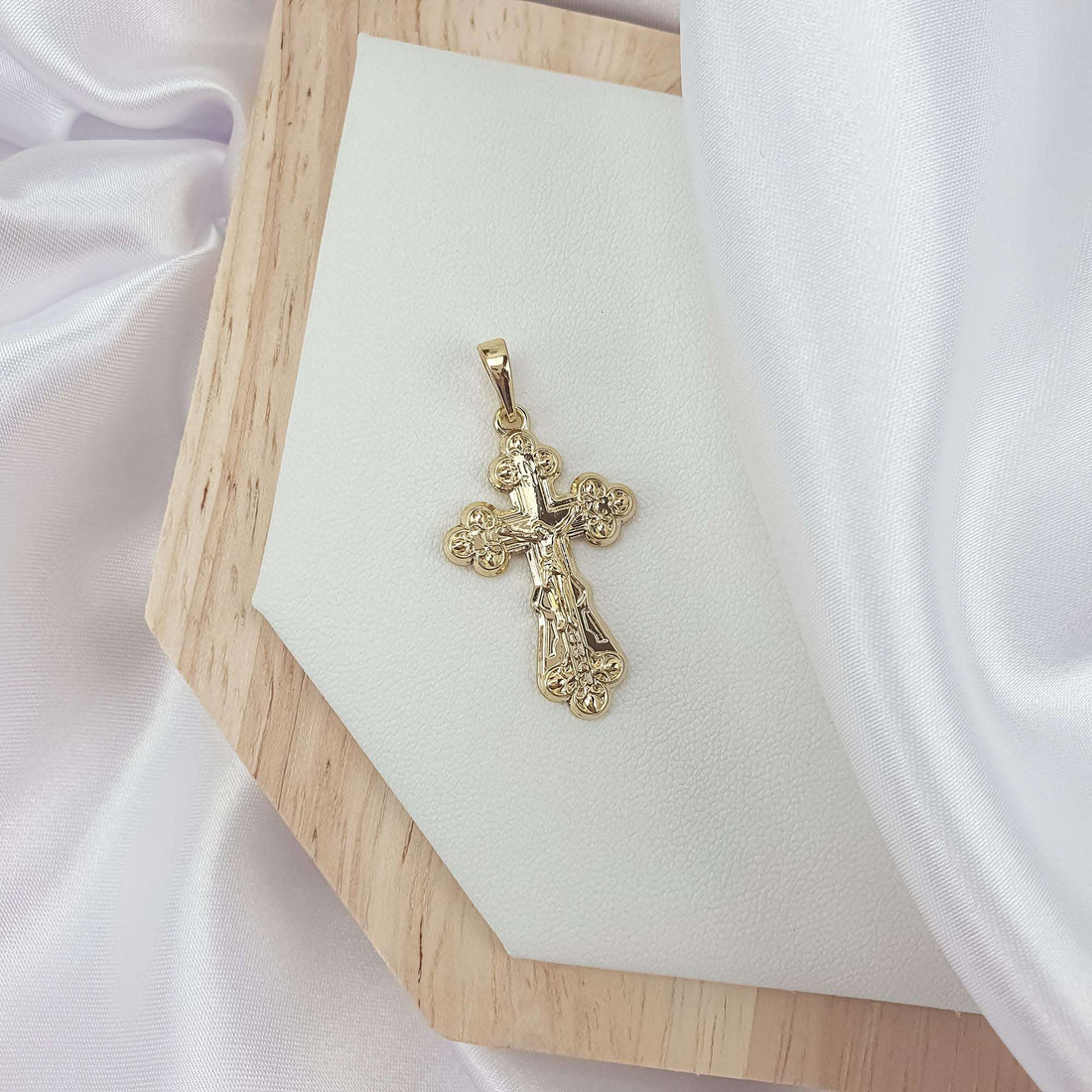 Apzeltīts krusts ar krucifiksa reljefu un ziedveida galiem uz koka dēlīša