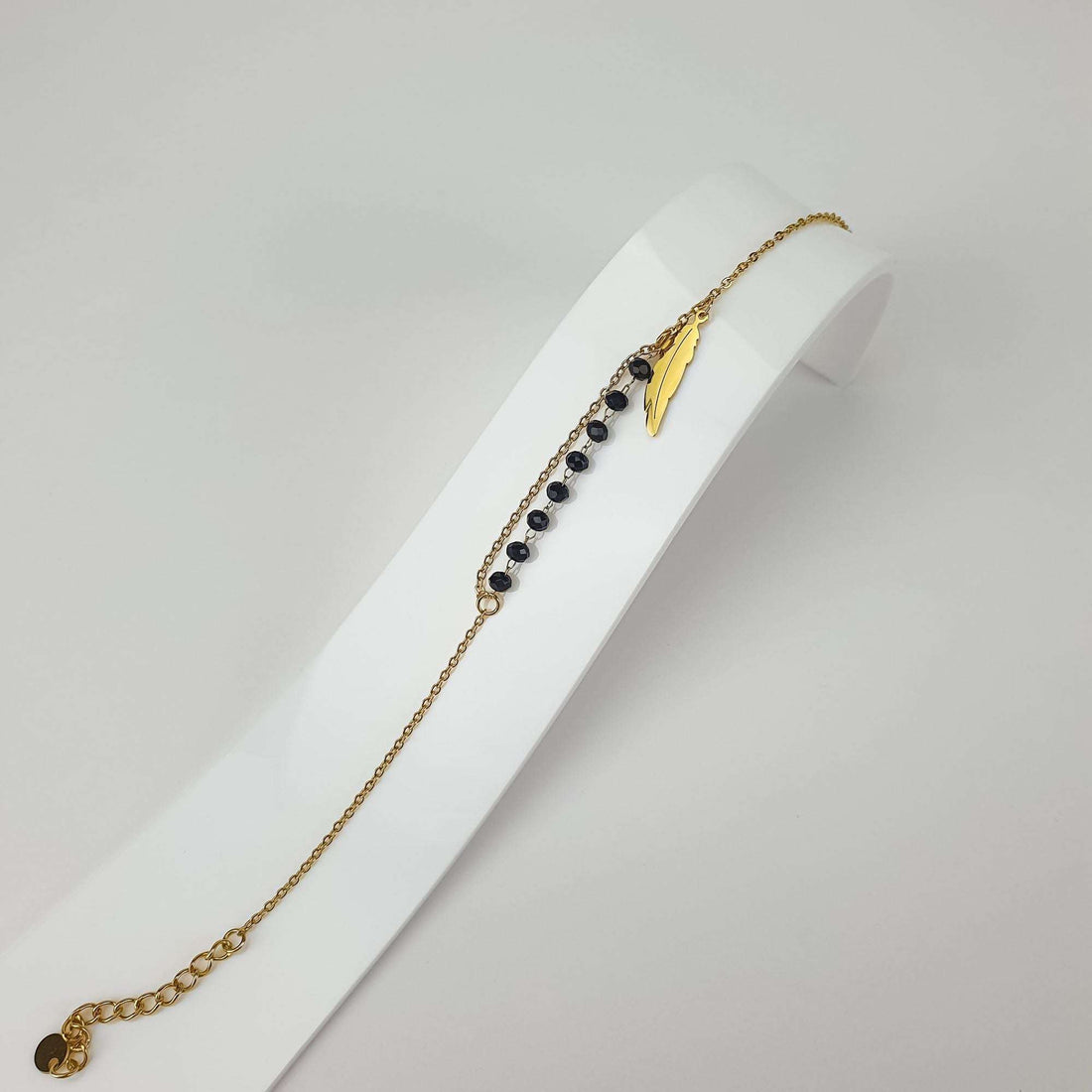 Spalvas piekariņa rokassprādze slīpā skatā uz balta statīva ar melnām fasētām pērlītēm